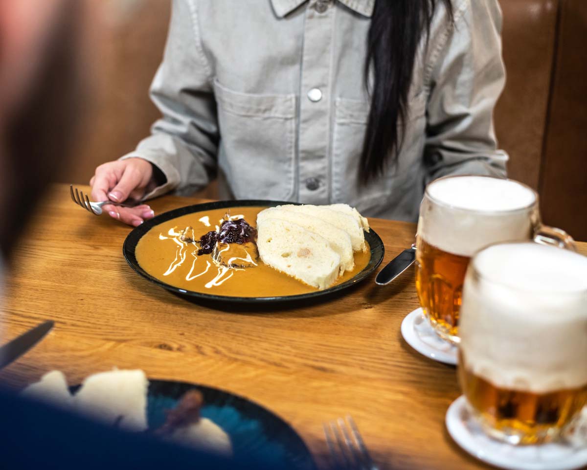 Zákazník si pochutnává na tradiční svičkové na smetaně, podávané s houskovým knedlíkem a brusinkami, v populární restauraci v Praze. Na stole také stojí dvě piva, ideální doplněk k české klasice.